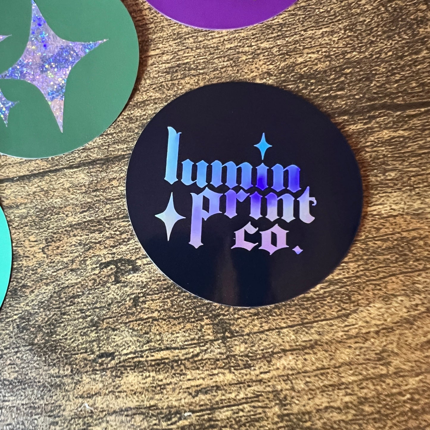 Black circular sticker with a colorful design on a wooden surface