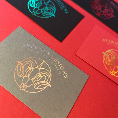 Business cards with silver foil logo on a red card, grey card and black card surface